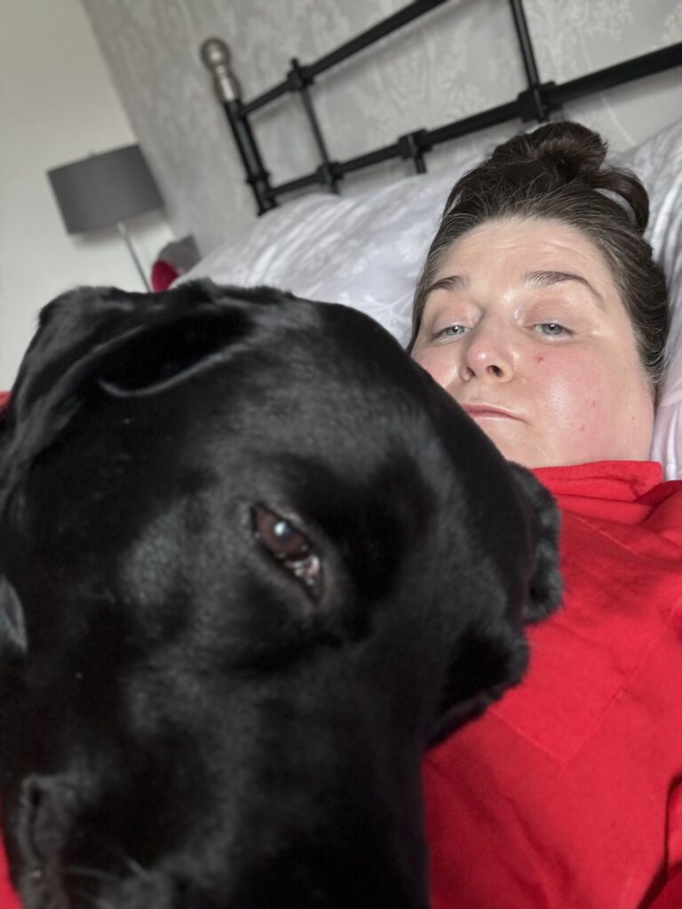 Alisha a dark haired woman wearing red pyjamas and being cuddled by her Black Labrador Alfie